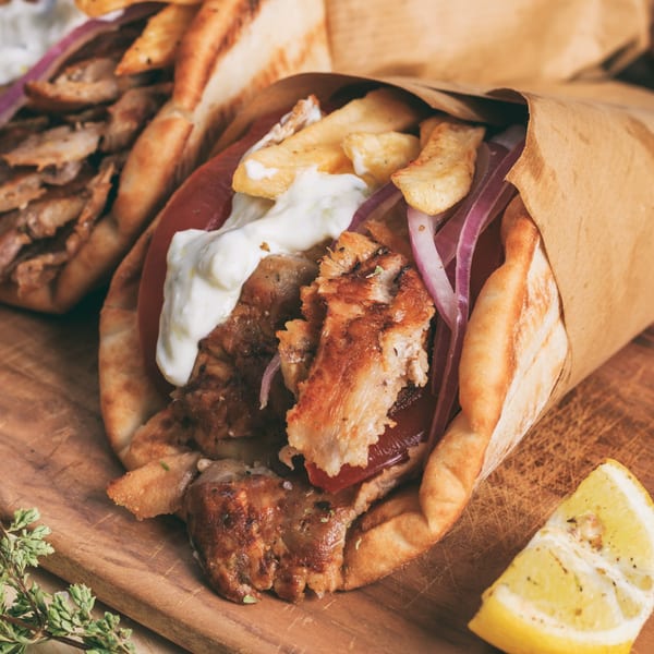 Close-up of a chicken gyro with fries, red onions, and sauce, wrapped in paper.