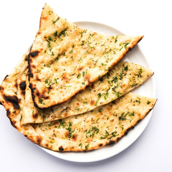 Golden-brown garlic naan bread, garnished with fresh herbs and spices, on a white plate.