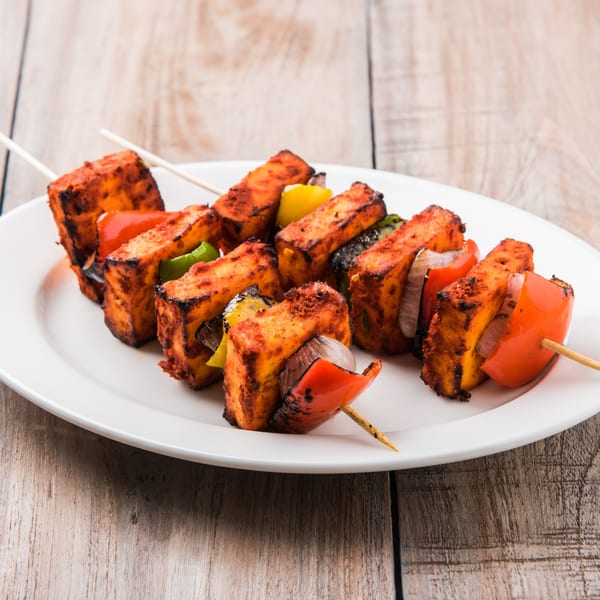 Paneer tikka skewers with red and yellow bell peppers and onions on a white plate.