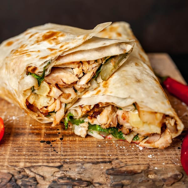 Two Indian chicken wraps with lettuce and sauce on a rustic wooden board with red peppers.